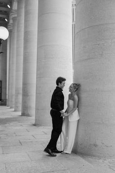 a man and woman standing next to each other in front of large pillars with lights on them