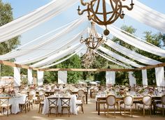 an outdoor wedding venue with white drapes and chandelier hanging from the ceiling