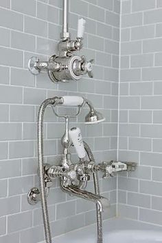 a bathtub with two faucets and three handset shower heads in a white tiled bathroom