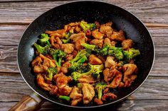 chicken and broccoli stir frying in a wok on a wooden table