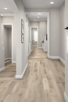 an empty hallway with hard wood floors and white trim on the walls, leading to another room