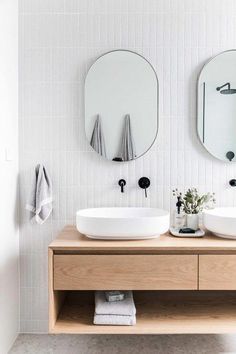 two white sinks sitting on top of a wooden counter next to mirrors and towel racks