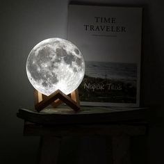 the moon lamp is on top of a table next to a book and an open book