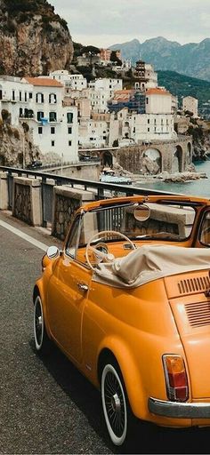 an orange car parked on the side of a road next to a body of water