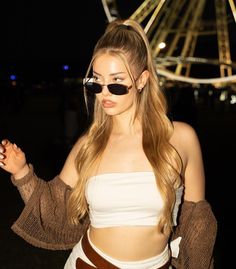 a woman with sunglasses on her face standing in front of a ferris wheel at night