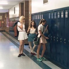 three girls are standing in front of lockers and looking at their cell phones while one girl is on her phone