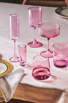 pink wine glasses are sitting on a table with plates and napkins next to them