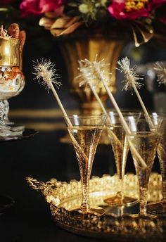 four champagne glasses with sparklers in them sitting on a gold tray next to flowers