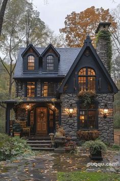 a stone house in the woods with lots of windows and plants on the front porch