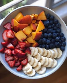 a white bowl filled with fruit and sliced bananas next to blueberries, peaches and strawberries