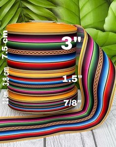 a stack of multicolored ribbons sitting on top of a wooden table next to green leaves