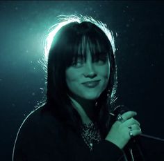 a woman holding a microphone in front of a dark background with light coming from behind her