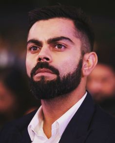 a man with a beard wearing a suit and looking off into the distance while standing in front of an audience