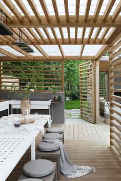 an outdoor dining area with white furniture and wood slats on the ceiling, along with wooden flooring