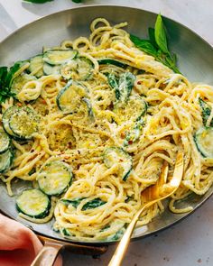 a pan filled with pasta and zucchini on top of a white countertop