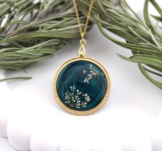 a necklace with flowers on it sitting next to some green leaves and branches in front of a white background