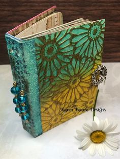 a small book with a flower on the side and a beaded charm attached to it