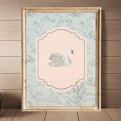 a white swan sitting on top of a wooden floor in front of a framed photo