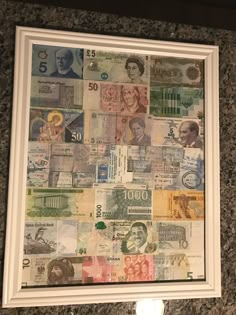 a white frame with lots of different currency on the wall next to a toilet paper dispenser