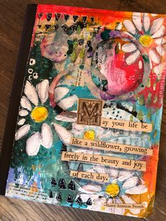 an art journal with flowers and words written on the pages, sitting on a wooden table