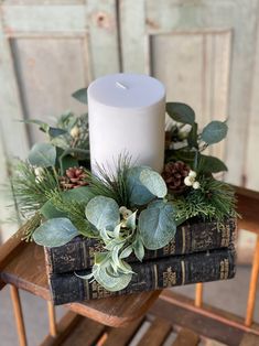 a white candle sitting on top of a stack of books with greenery and pine cones