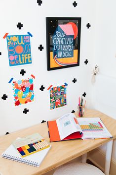 a wooden desk topped with lots of books and art work next to a white wall