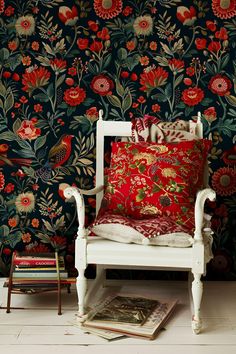 a white chair sitting in front of a wall with red and green flowers on it