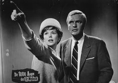 an old black and white photo of a man and woman pointing at something on the wall