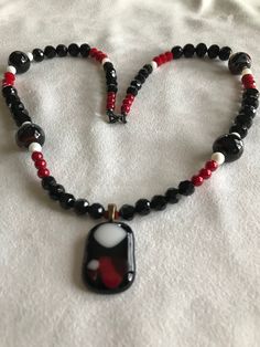 Black,red and white glass fused pendant highlight this beaded necklace which include four multi colored marble shaped beads. Black Glass Beaded Necklace With Colorful Beads, Black Glass Beaded Necklaces With Colorful Beads, Black Glass Round Bead Jewelry, Black Glass Round Beads Jewelry, Black Glass Jewelry With Large Beads, Black Glass Polished Beads Jewelry, Black Glass Jewelry With Polished Beads, Unique Red Glass Necklace, Black Jewelry With Colorful Czech Glass Beads