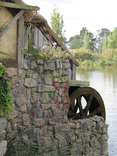 an old water wheel sitting on top of a stone wall next to a body of water