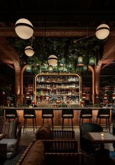 a dimly lit bar with lots of stools and plants hanging from the ceiling above it