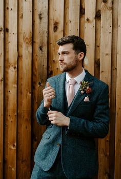 a man wearing a suit and tie standing in front of a wooden fence with his hands clasped