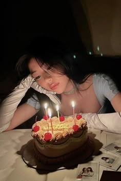 a woman sitting in front of a cake with lit candles on it and looking at the camera