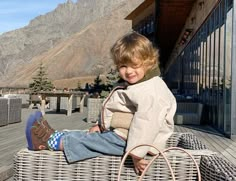 a young boy sitting on top of a wicker bench next to a mountain range