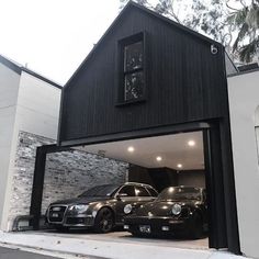 two cars are parked in front of a black garage with an open door on the side