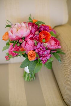 a bouquet of pink and orange flowers sitting on a couch next to a white pillow