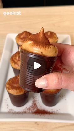 a hand holding a chocolate cupcake in front of some other cupcakes on a white plate