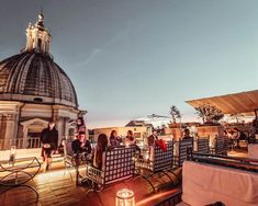 people sitting at tables on the roof of a building with a dome in the background