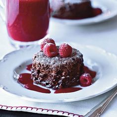 a piece of chocolate cake with raspberries on top and a glass of juice