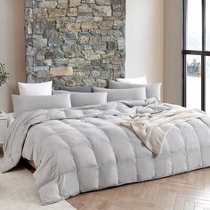 a large bed sitting next to a stone wall in a room with wooden floors and windows