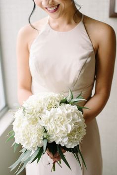 a woman in a dress holding a bouquet of white flowers and smiling at the camera