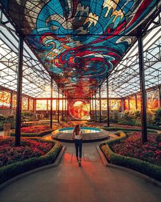 a woman standing in the middle of a building with lots of plants and flowers around it