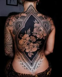 the back of a woman's body with tattoos and flowers on her upper half