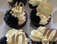 four cupcakes with white frosting and black icing are arranged in a box