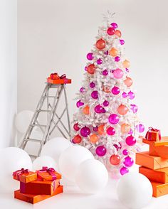 a white christmas tree with orange and pink ornaments in front of presents on the floor