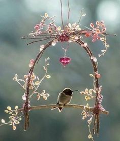 a small bird sitting on top of a branch with flowers and hearts hanging from it