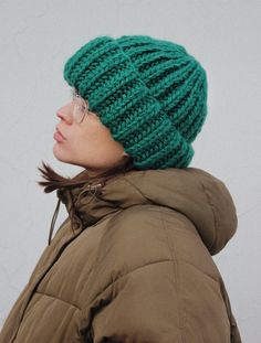 a woman wearing a green knitted beanie hat and glasses looking off into the distance