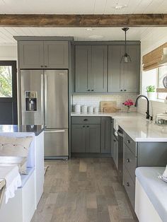 a kitchen with gray cabinets and white counter tops, along with wood flooring that matches the ceiling