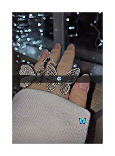 a person's hand with two rings on it and a butterfly brooch in the middle