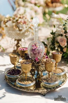 there is a glass bottle with flowers in it on the table next to cups and saucers